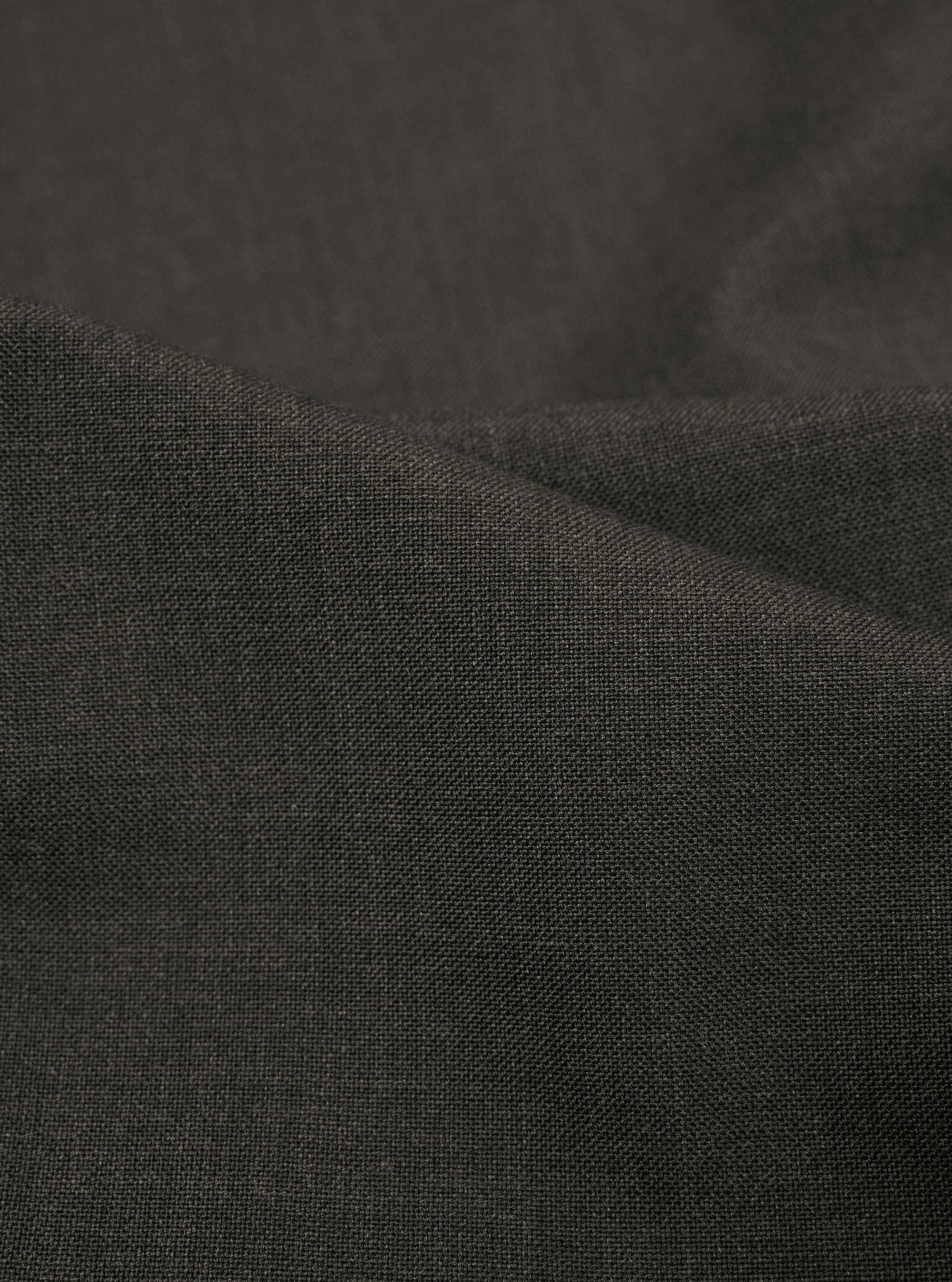 A detailed, close-up fabric swatch of the Olive Marl Tropical Suiting Pleated Track Pant shows the fine, textured weave of the olive green material.