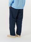 A model is wearing the Navy Chester Stripe Oxford Pant against a plain white background. The image, taken from a side-rear perspective, showcases the loose, wide-leg fit of the navy blue trousers, which feature thin vertical white stripes and a single rear buttoned pocket.
