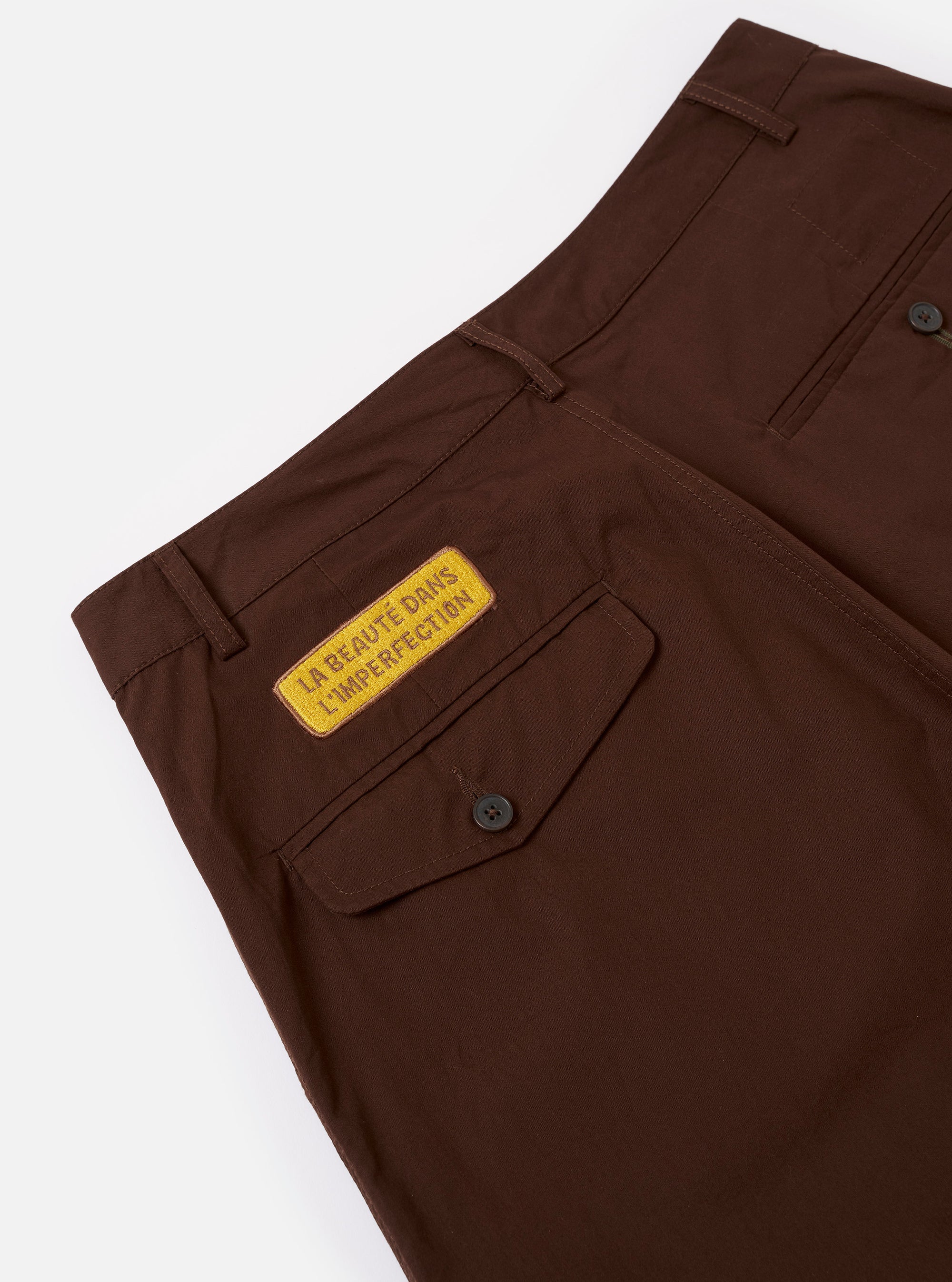 The Paraboot x Universal Works Brown Peached Poplin Super Chino is shown from a rear angle as a flat lay against a plain white background. The image highlights the two rear pockets, including one with a button-down flap, and the elasticated waistband. The rich brown peached poplin fabric features visible stitching details and a smooth texture.