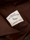 The Paraboot x Universal Works Brown Peached Poplin Super Chino is shown from a rear angle as a flat lay against a plain white background. The image highlights the two rear welt pockets, a small collaborative brand label above the right pocket, and the smooth, peached texture of the brown cotton poplin fabric.