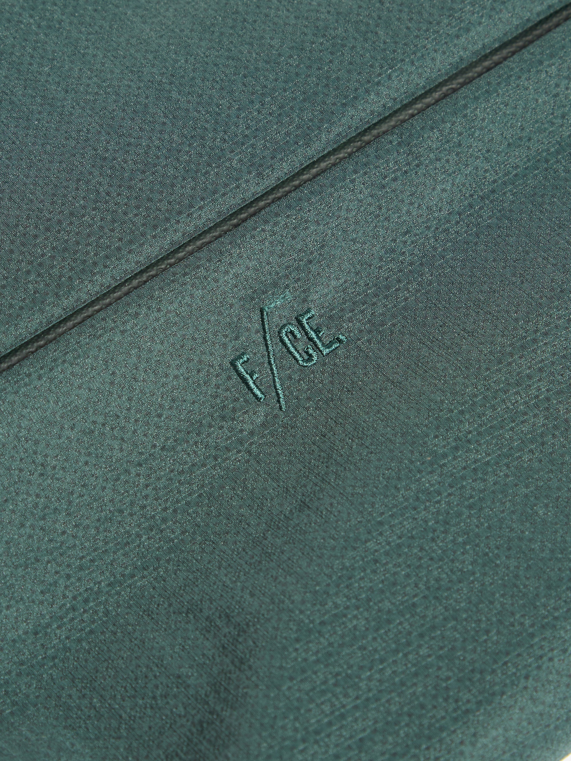 Close-up of the F/CE.® Green Nylon 2.5 Layer Sacoche showing the fabric texture and embroidered logo. The background is a simple, neutral surface.