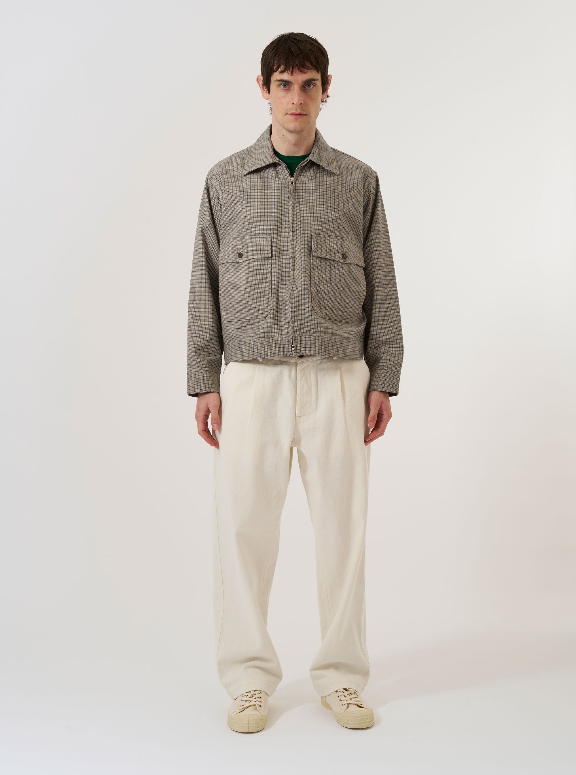 A model wears the Multi Lucas Cotton Mix E130 Jacket over a light-colored shirt and dark trousers, standing against a plain white background. The jacket features a bold, multi-colored check pattern in shades of blue, brown, and cream. It is designed with a classic collar, a two-way front zip closure, and two large flap pockets at the waist. The model is shown from a front angle, highlighting the garment's relaxed, boxy fit.