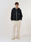 A model wears the Ecru Slub Drill Duke Pant against a plain, light grey background. The trousers are shown from the front, featuring a loose, wide-leg fit with visible pleats at the waist and a cream-colored fabric with a subtle slub texture. The model is also wearing a light-colored shirt and dark shoes.