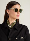 Model wearing A. SOCIETY x Universal Works Honey Stanley Sunglasses. The sunglasses have a light honey-colored frame and dark lenses. Shot in a studio with a plain background.