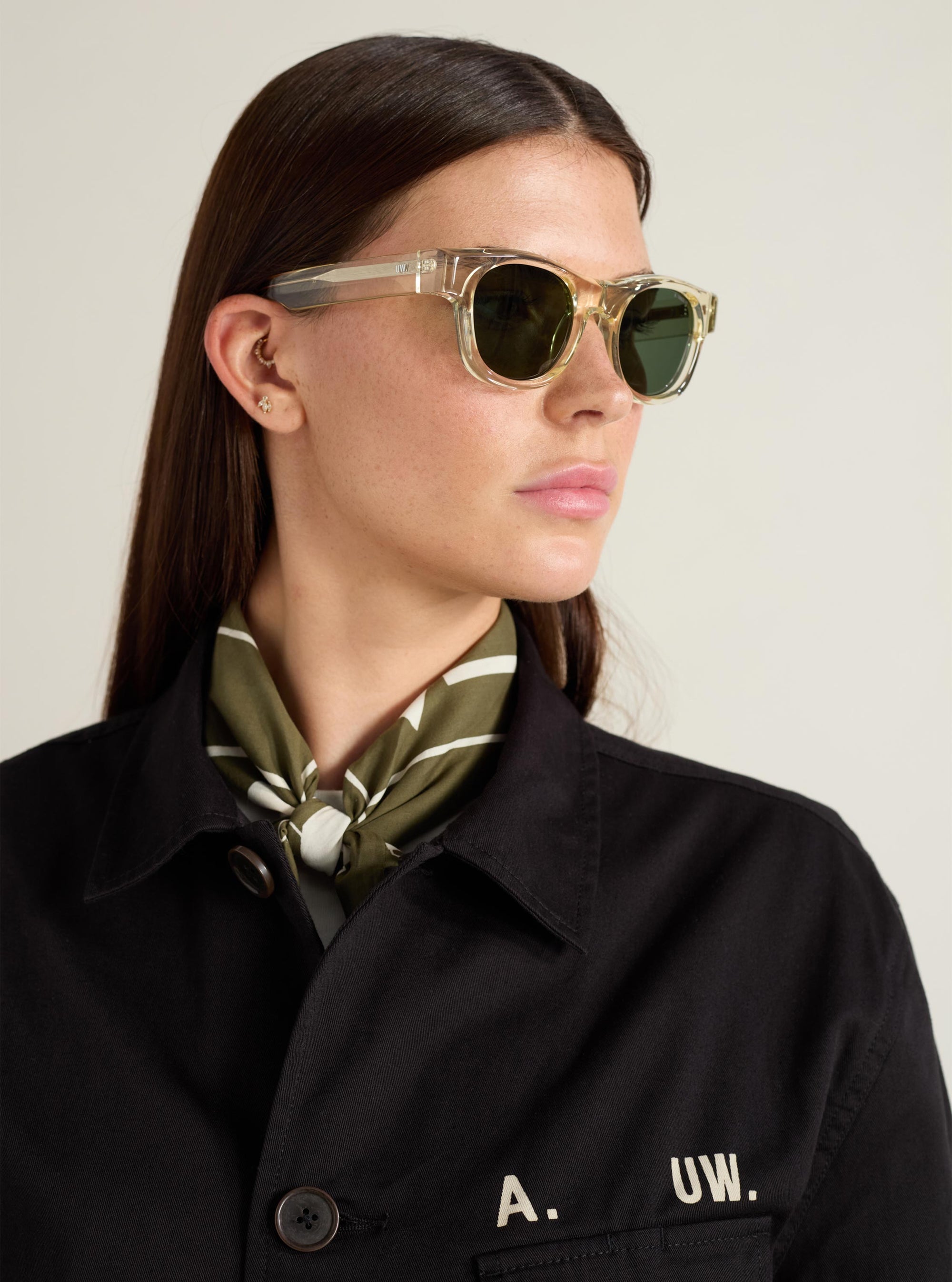 Model wearing A. SOCIETY x Universal Works Honey Stanley Sunglasses. The sunglasses have a light honey-colored frame and dark lenses. Shot in a studio with a plain background.