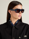 Model wearing A. SOCIETY x Universal Works Navy Aberdeen Sunglasses. The sunglasses have a thick navy frame and brown lenses. Shot in a studio with a neutral background.