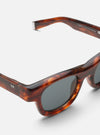 Close-up of A. SOCIETY x Universal Works Brown Stanley Sunglasses on a white surface. The brown tortoiseshell frame and grey lenses are clearly visible.