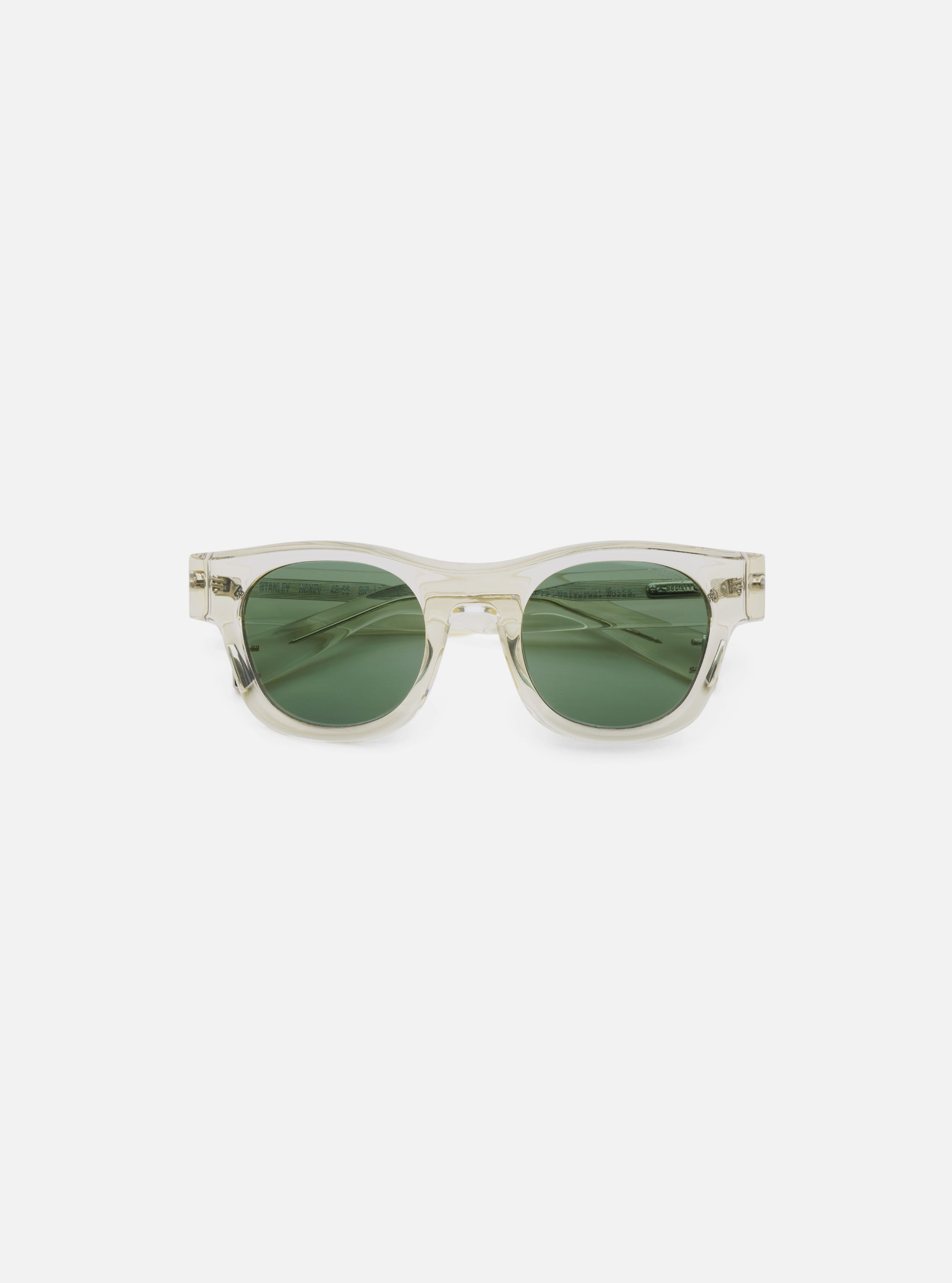 Close-up of A. SOCIETY x Universal Works Honey Stanley Sunglasses. Clear frame, green lenses. Shot on a clean white background.