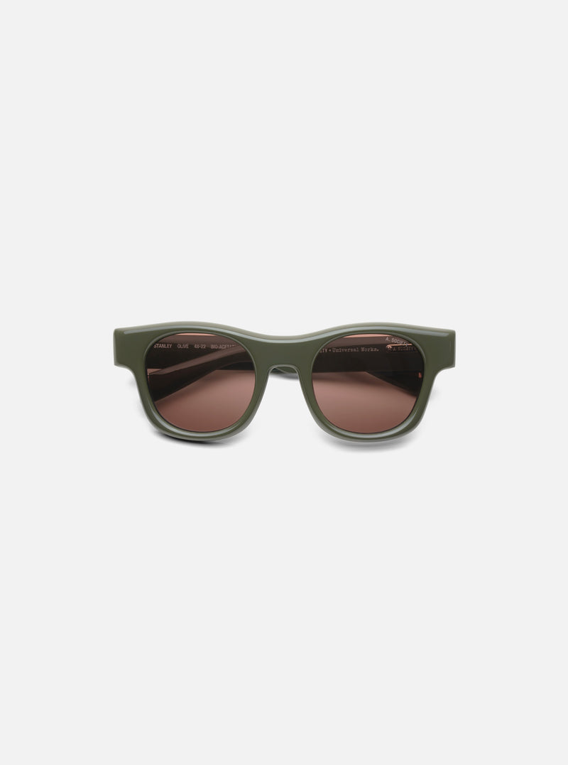 A. SOCIETY x Universal Works Olive Stanley Sunglasses on a white background. The frames are olive green and the lenses are brown.