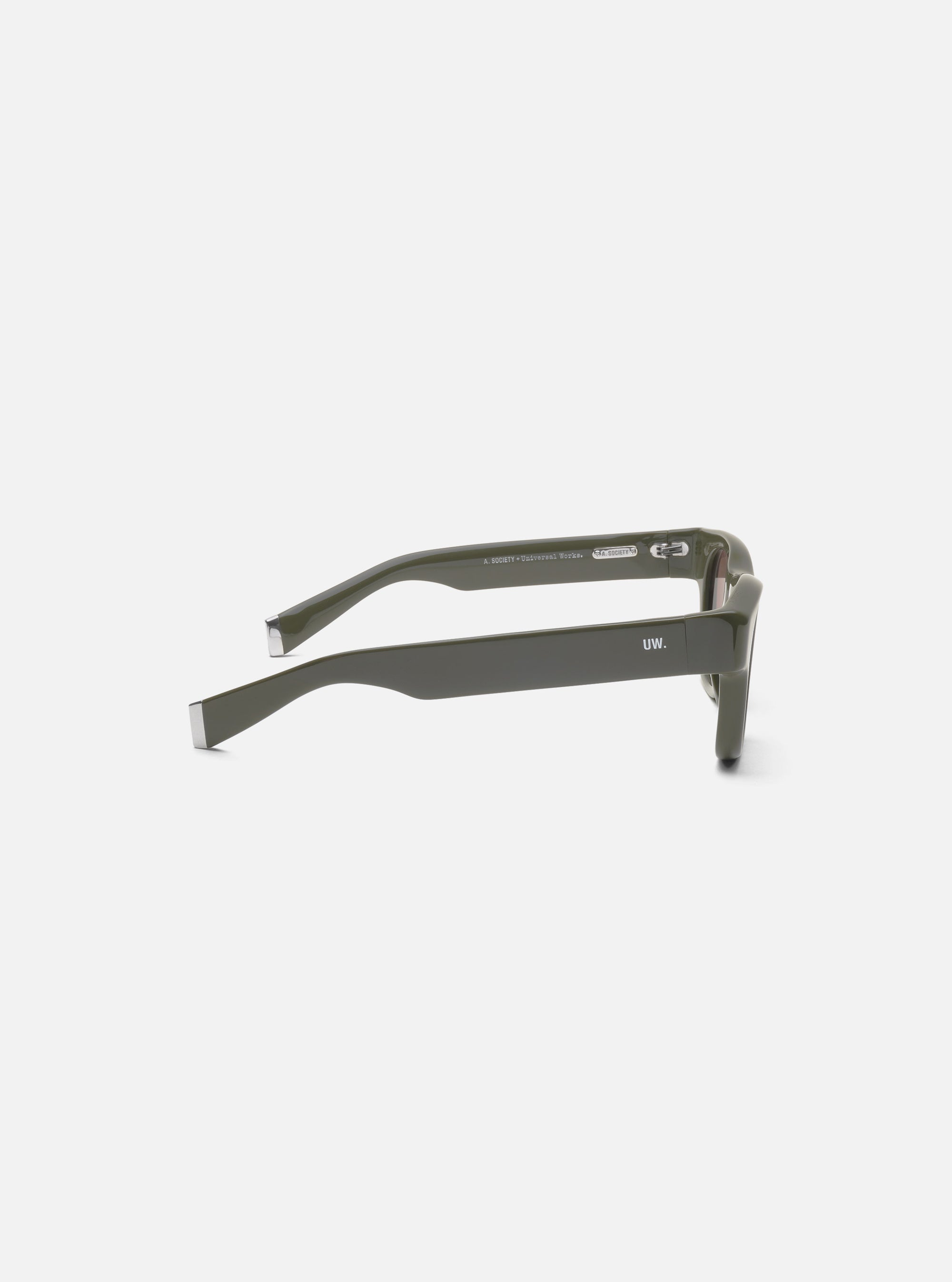 Side view of A. SOCIETY x Universal Works Olive Stanley Sunglasses on a white surface. Olive frames with silver accents. "UW." printed on the side.