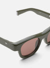 Close-up of A. SOCIETY x Universal Works Olive Stanley Sunglasses on a white surface. Olive frames, brown lenses. Modern, stylish eyewear.