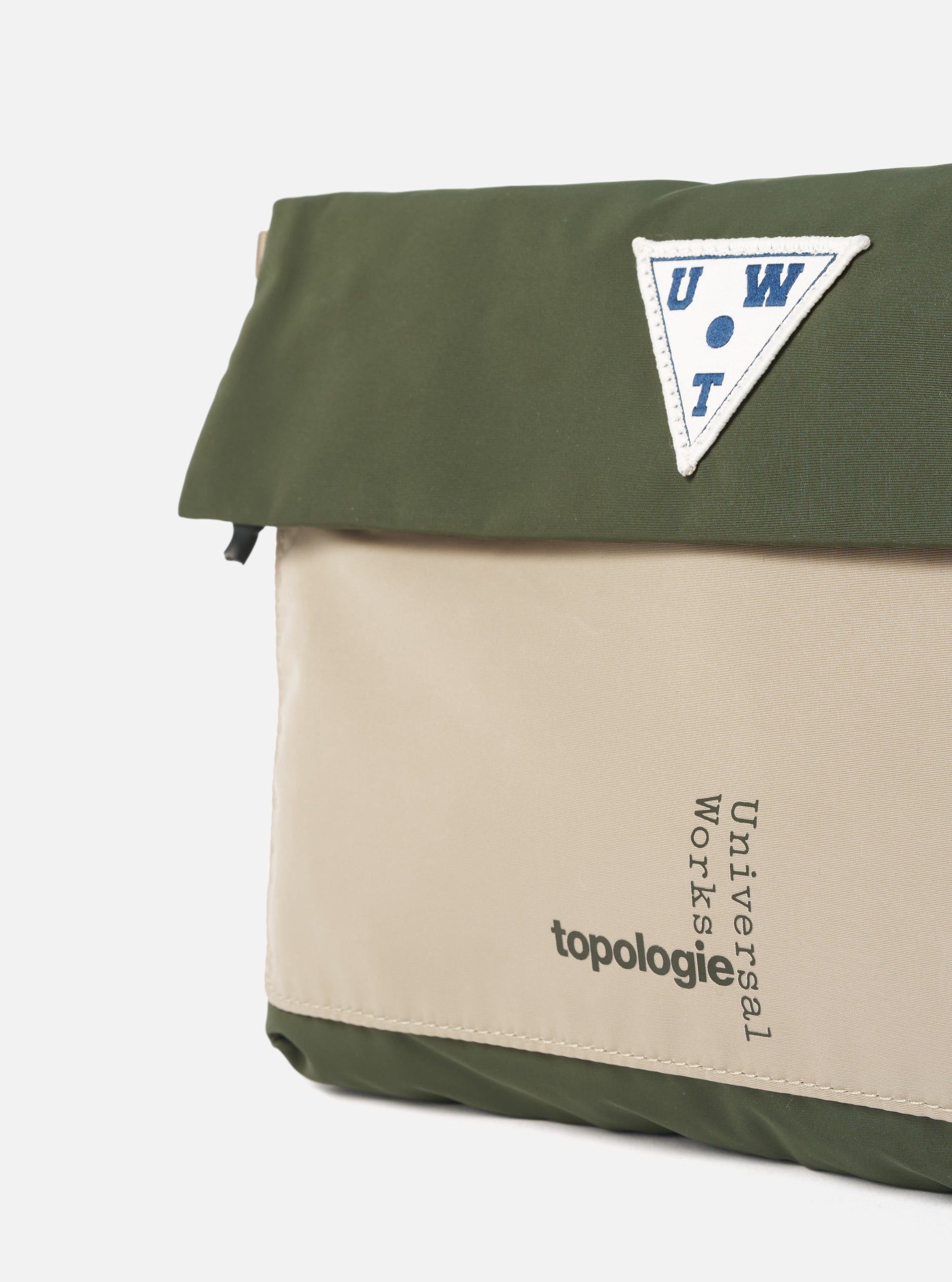 Close-up of the Topologie x Universal Works Rifle Green UW Tech Musette Medium bag. Features a green and beige color block design with the logos. Shot on a white background.