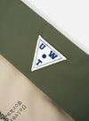 Close-up of the Topologie x Universal Works Rifle Green UW Tech Musette Medium bag. Features a green and beige color block design with a UW logo patch. Shot on a white background.