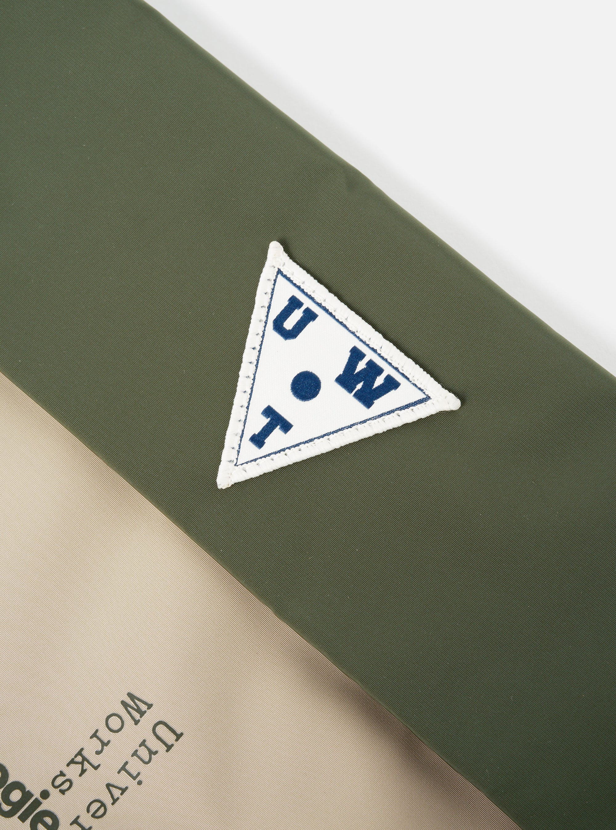 Close-up of the Topologie x Universal Works Rifle Green UW Tech Musette Medium bag. Features a green and beige color block design with a UW logo patch. Shot on a white background.