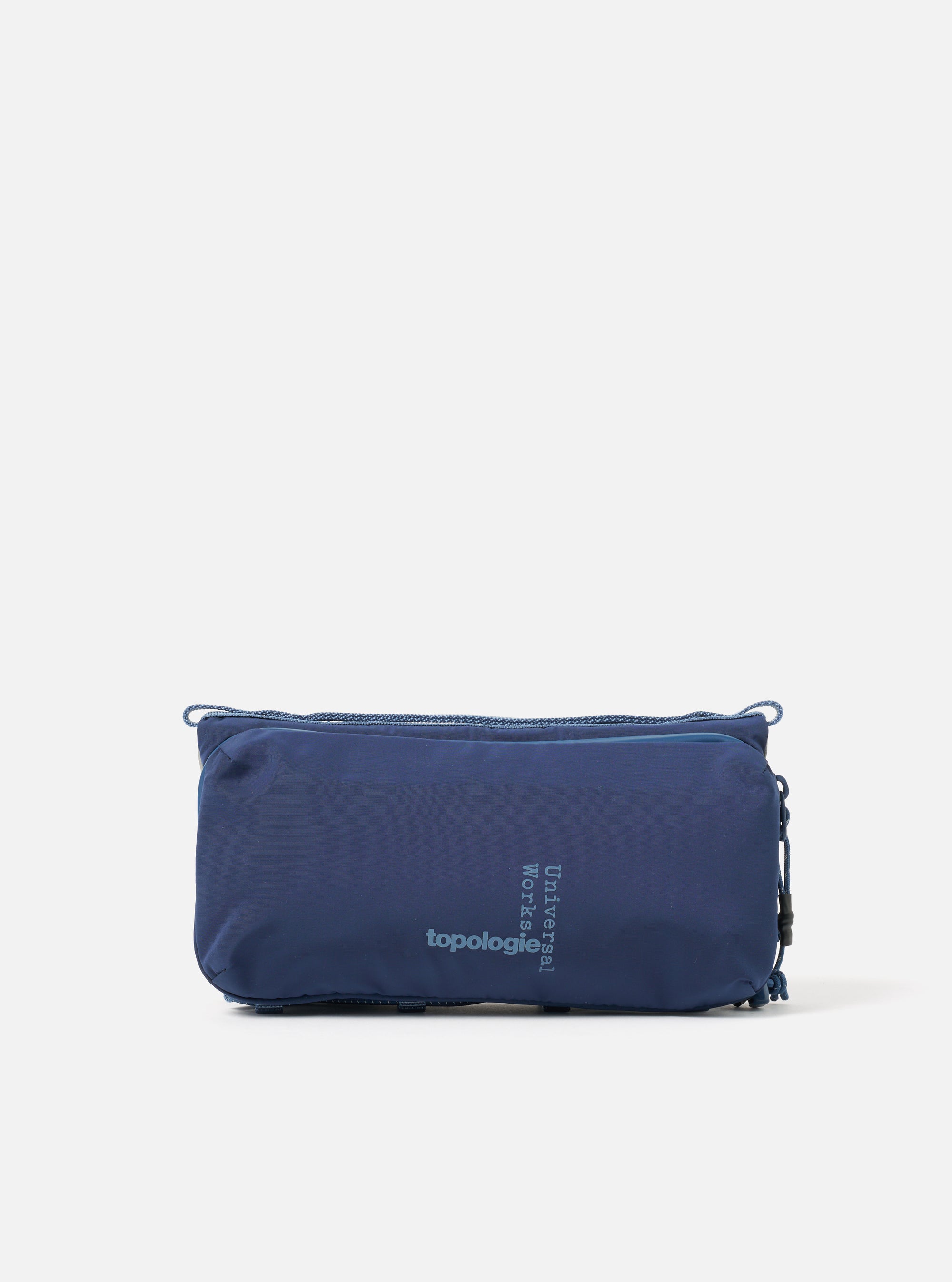 Topologie x Universal Works Insignia Blue UW Tech Bottle Sacoche Medium on a white background. The blue bag features a zip closure and drawstring detail.