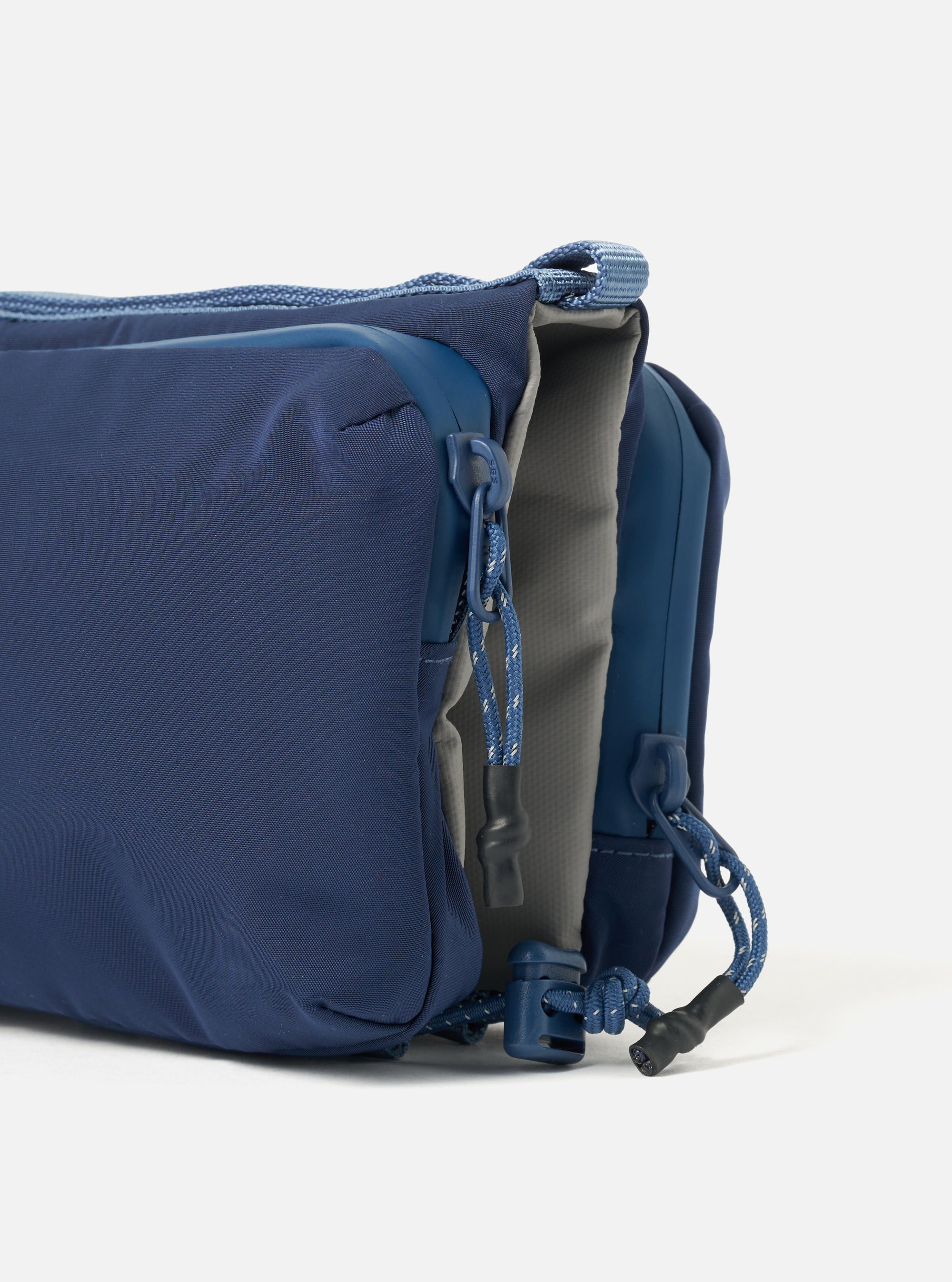 Close-up of the Topologie x Universal Works Insignia Blue UW Tech Bottle Sacoche Medium. The blue bag features a gray interior and blue zipper pulls. Shot on a white background.