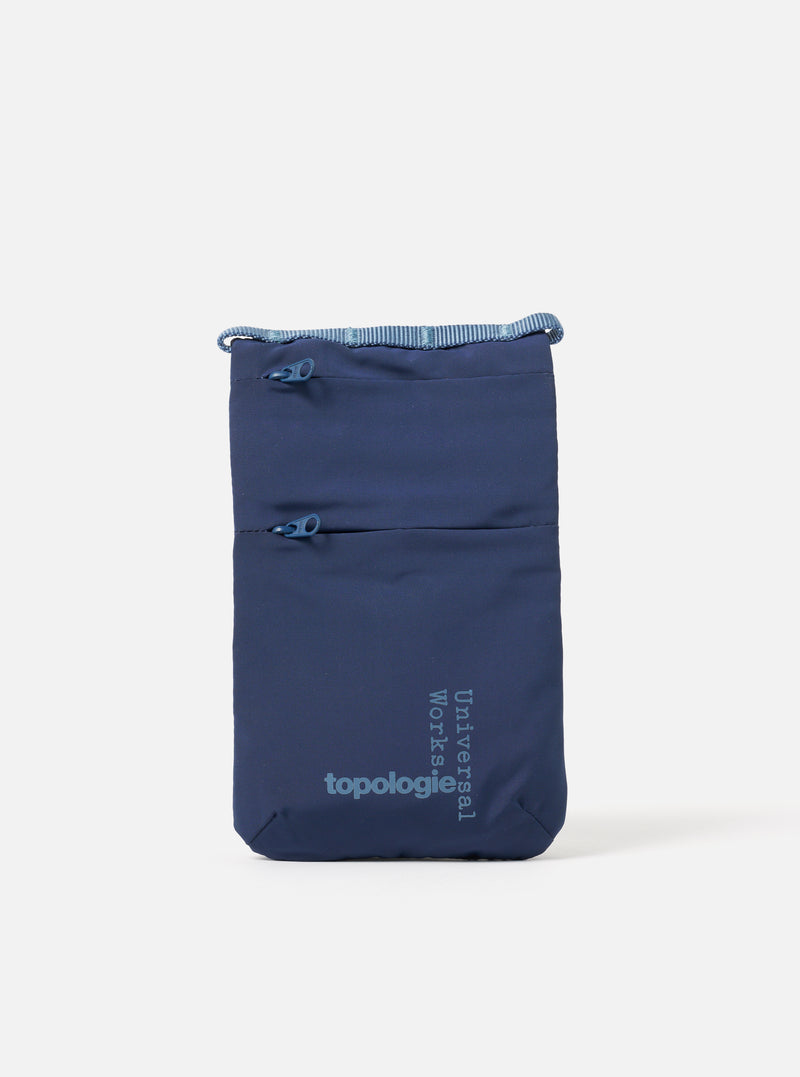 The Topologie x Universal Works Insignia Blue UW Tech Phone Sacoche on a white background. The blue bag has two zipped pockets and logos for both brands.