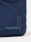 Close-up of the Topologie x Universal Works Insignia Blue UW Tech Phone Sacoche. The blue fabric bag features the brand logos in a lighter blue. Shot against a white background.
