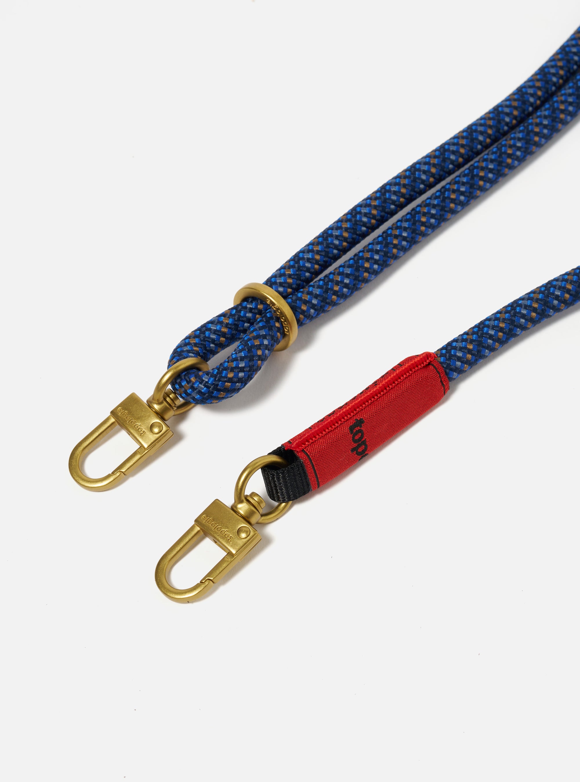 Close-up of the Topologie x Universal Works Navy Hitch UW Rope 8mm Rope Strap on a white background. The strap is blue with gold hardware and a red accent.