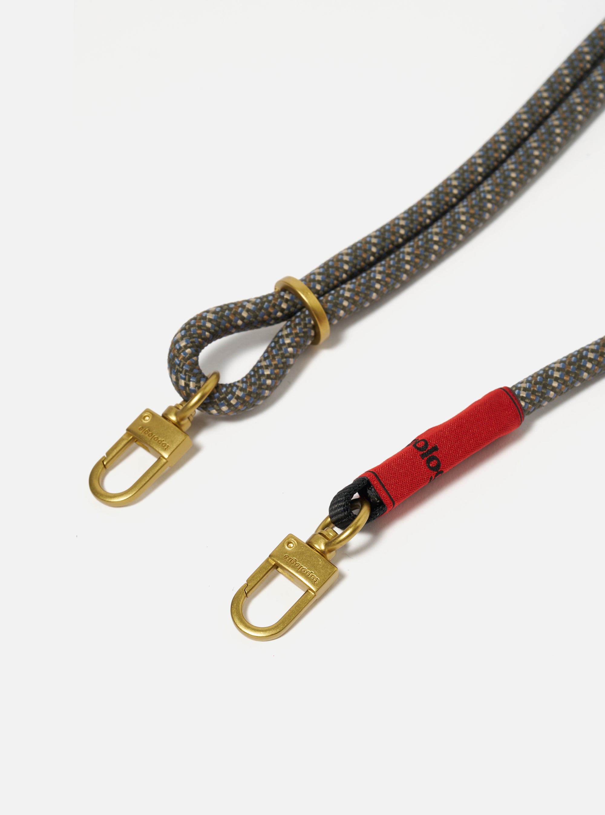 Close-up of the Topologie x Universal Works Red Hitch UW Rope 8mm Strap on a white background. The rope is patterned with blue, brown and grey, and has gold-colored clasps.