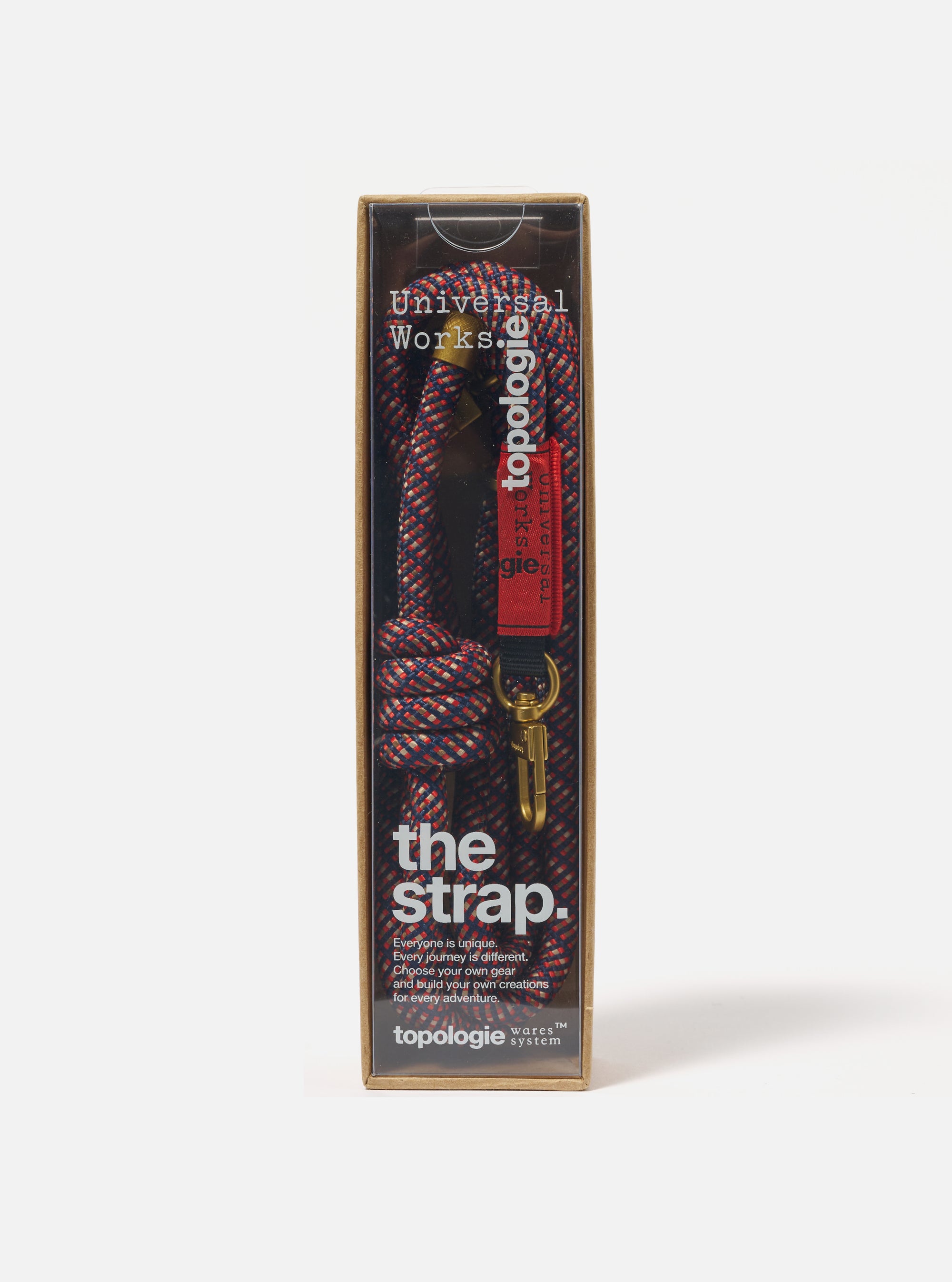 Topologie x Universal Works Olive Hitch UW Rope 8mm Rope Strap in its packaging. The rope is red, blue and beige. The packaging is brown and clear. Studio shot on a white background.