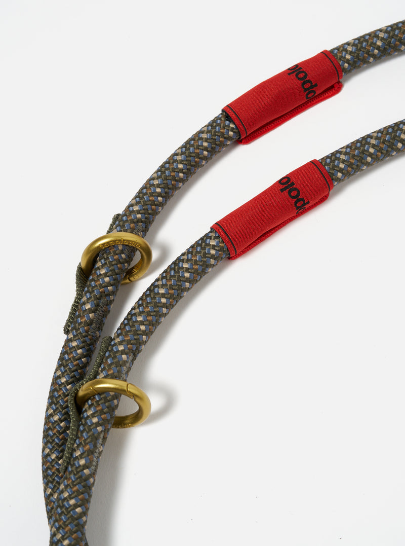 Close-up of the Topologie x Universal Works Olive Hitch UW Rope 10mm Loop on a white surface. The rope is olive, blue, and brown with red fabric and gold rings.