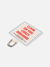 Close-up of the Topologie x Universal Works Off White UW Tech Phone Strap Adapter. It's off-white with red text and a blue border, featuring a silver metal clip. Shot on a clean white background.
