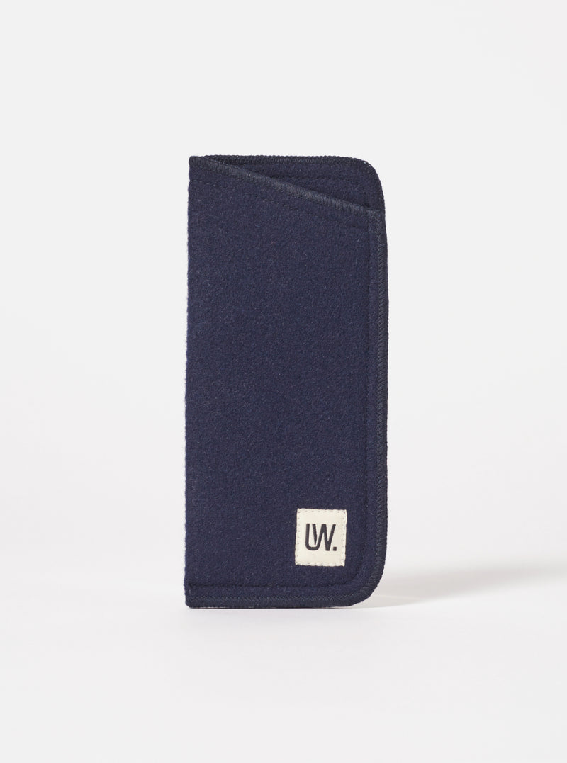 Close-up of a Navy Melton Large Glasses Case on a white background. The case is made of navy blue melton wool and has a small white tag with the letters 'UW' on it.