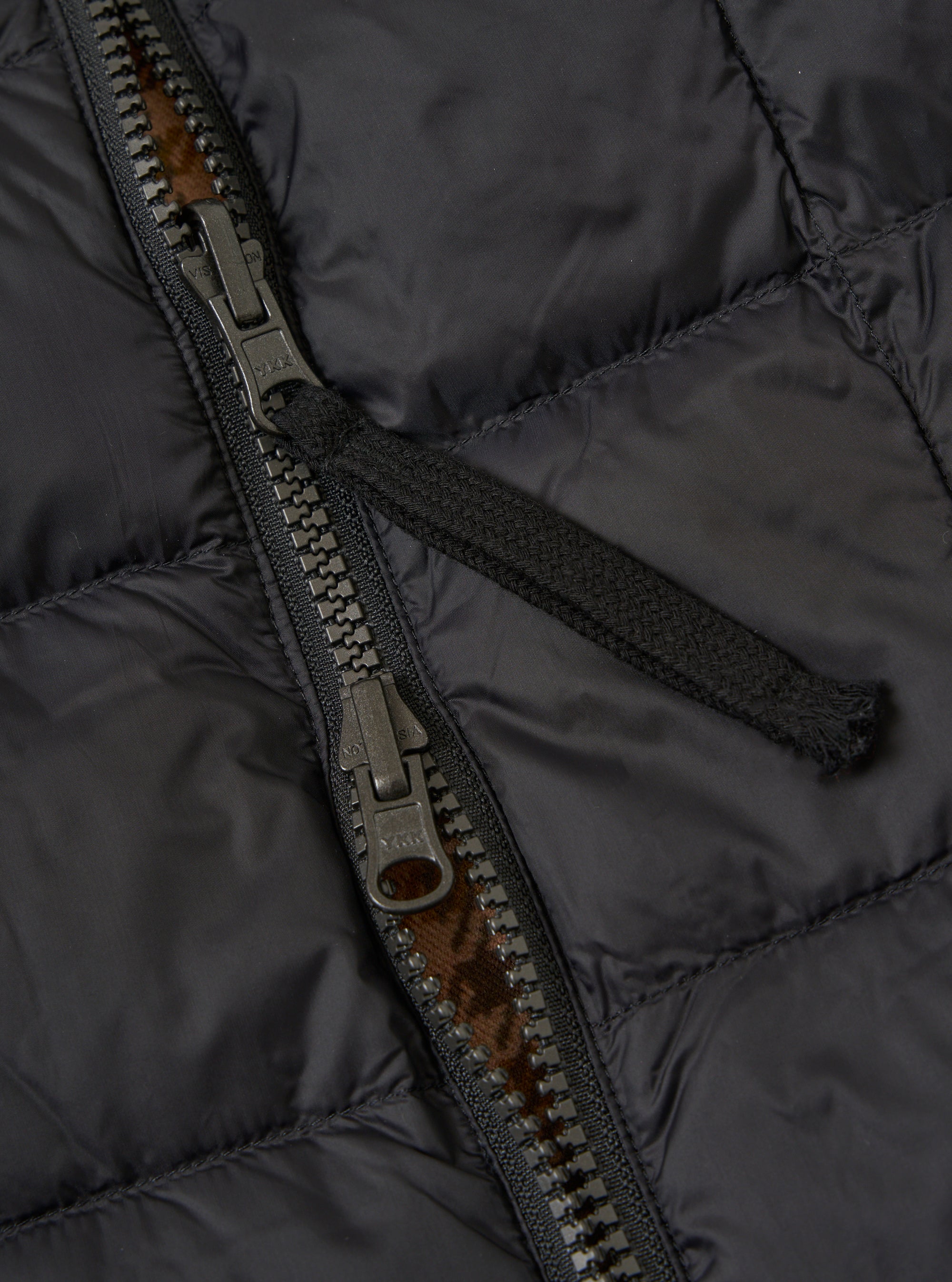 Close-up of the TAION x Universal Works Reversible Black Military Line Vest, showcasing the black quilted material and zipper detail. 