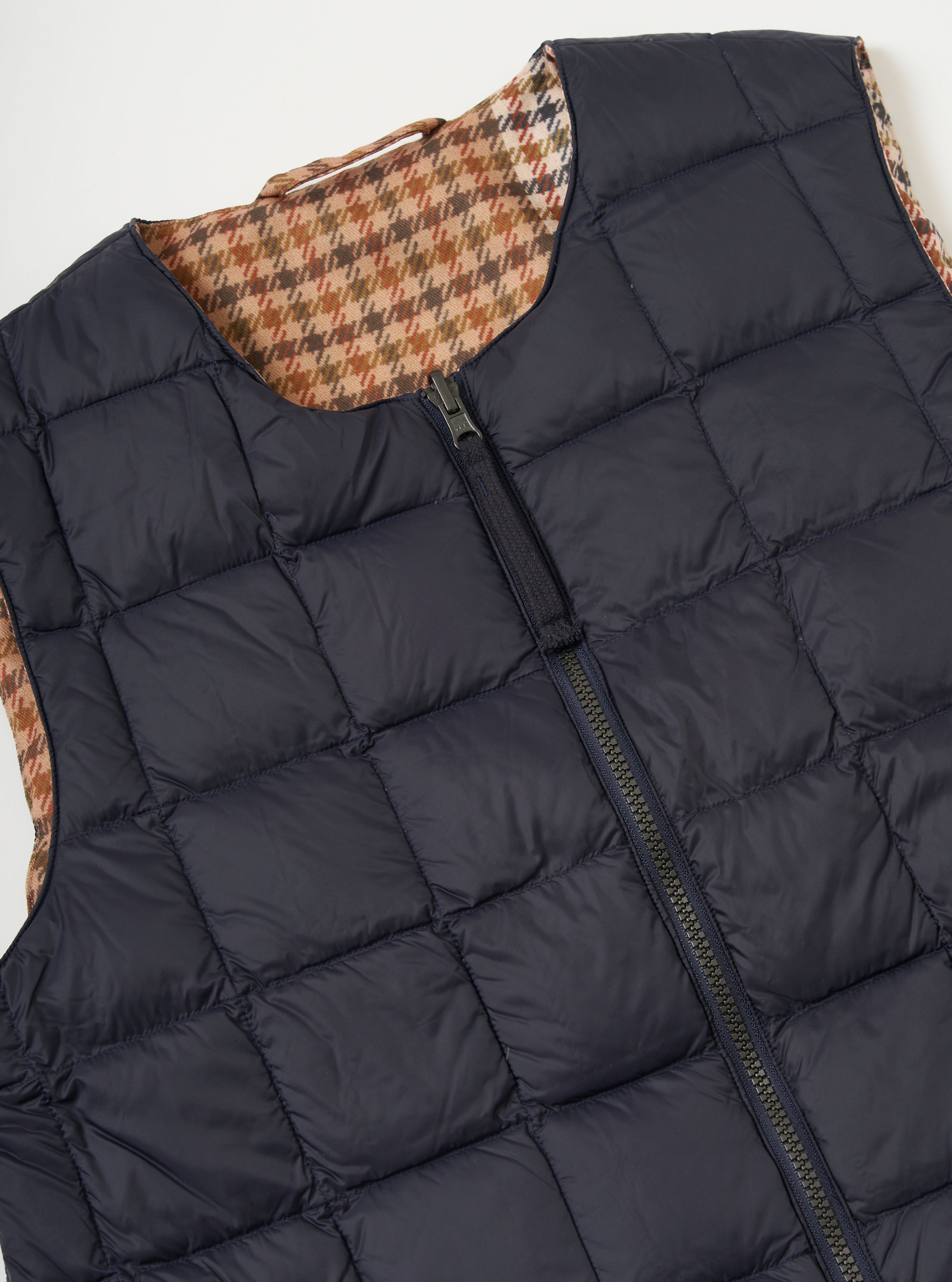 Close-up of the TAION x Universal Works Reversible Dark Navy Military Line Vest on a white background. Shows the dark navy quilted side with a zipper and the brown houndstooth patterned reverse.