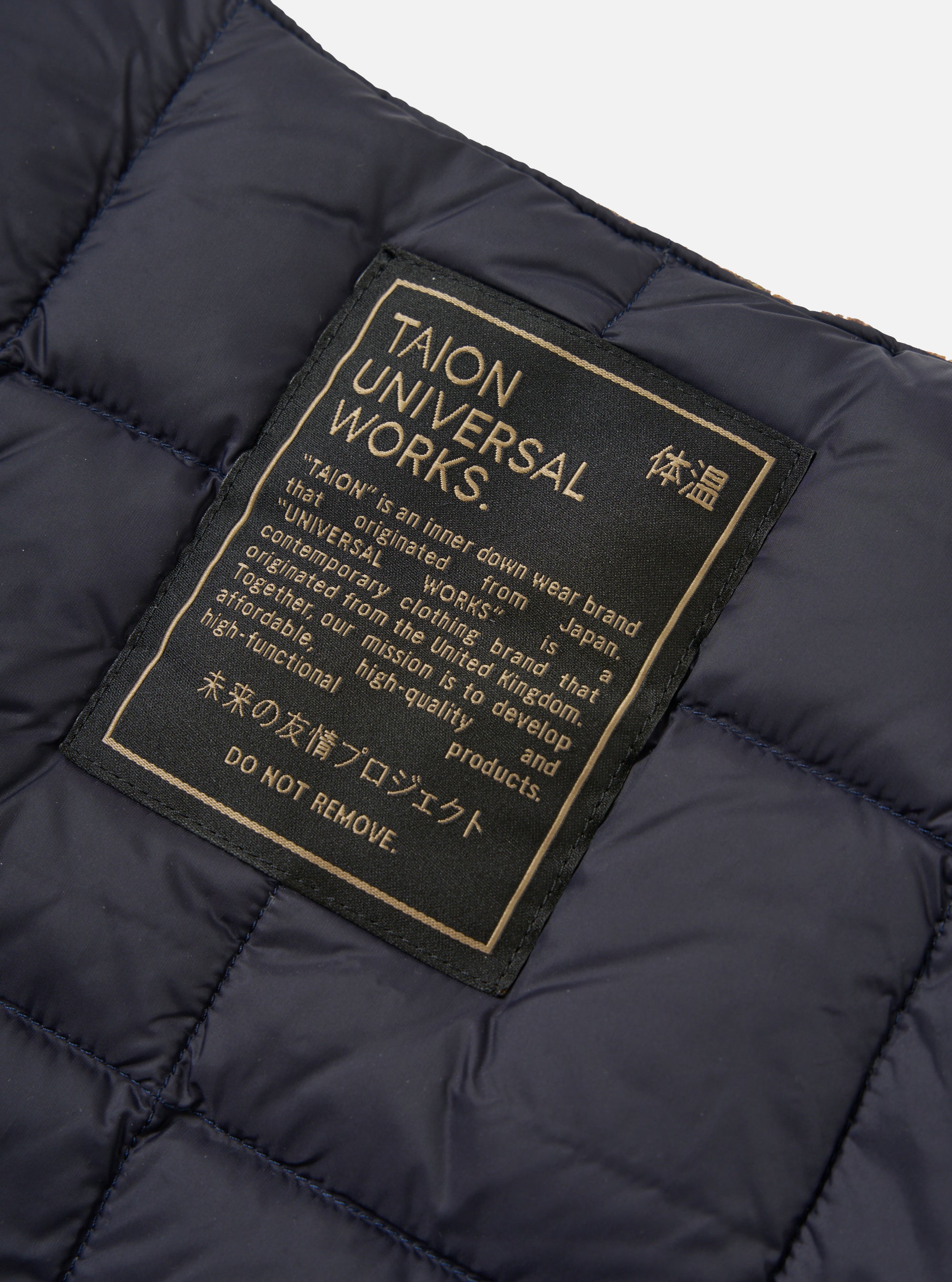 Close-up of the TAION x Universal Works Reversible Dark Navy Military Line Vest, showing the quilted texture and branded tag on a white background.