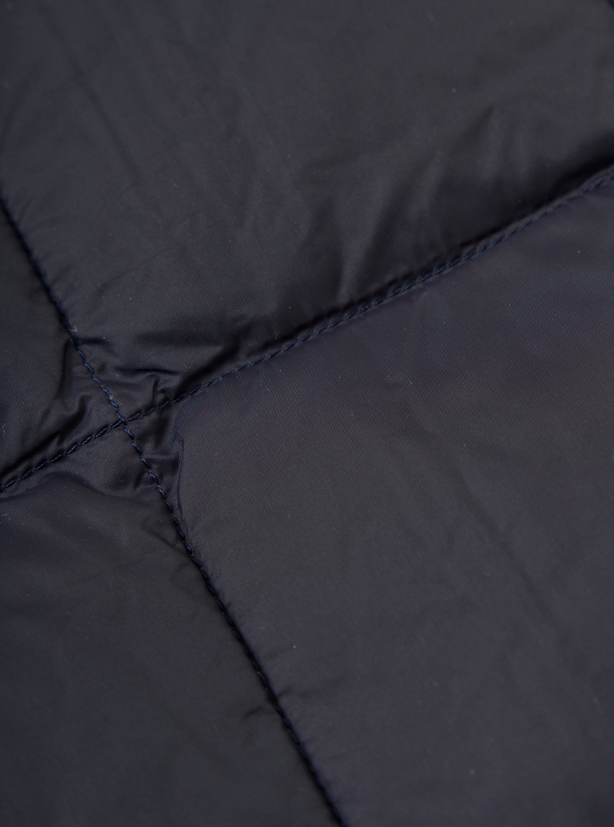 Close-up of the TAION x Universal Works Reversible Dark Navy Military Line Vest, showing the quilted texture and dark navy color. The fabric is smooth with subtle stitching.