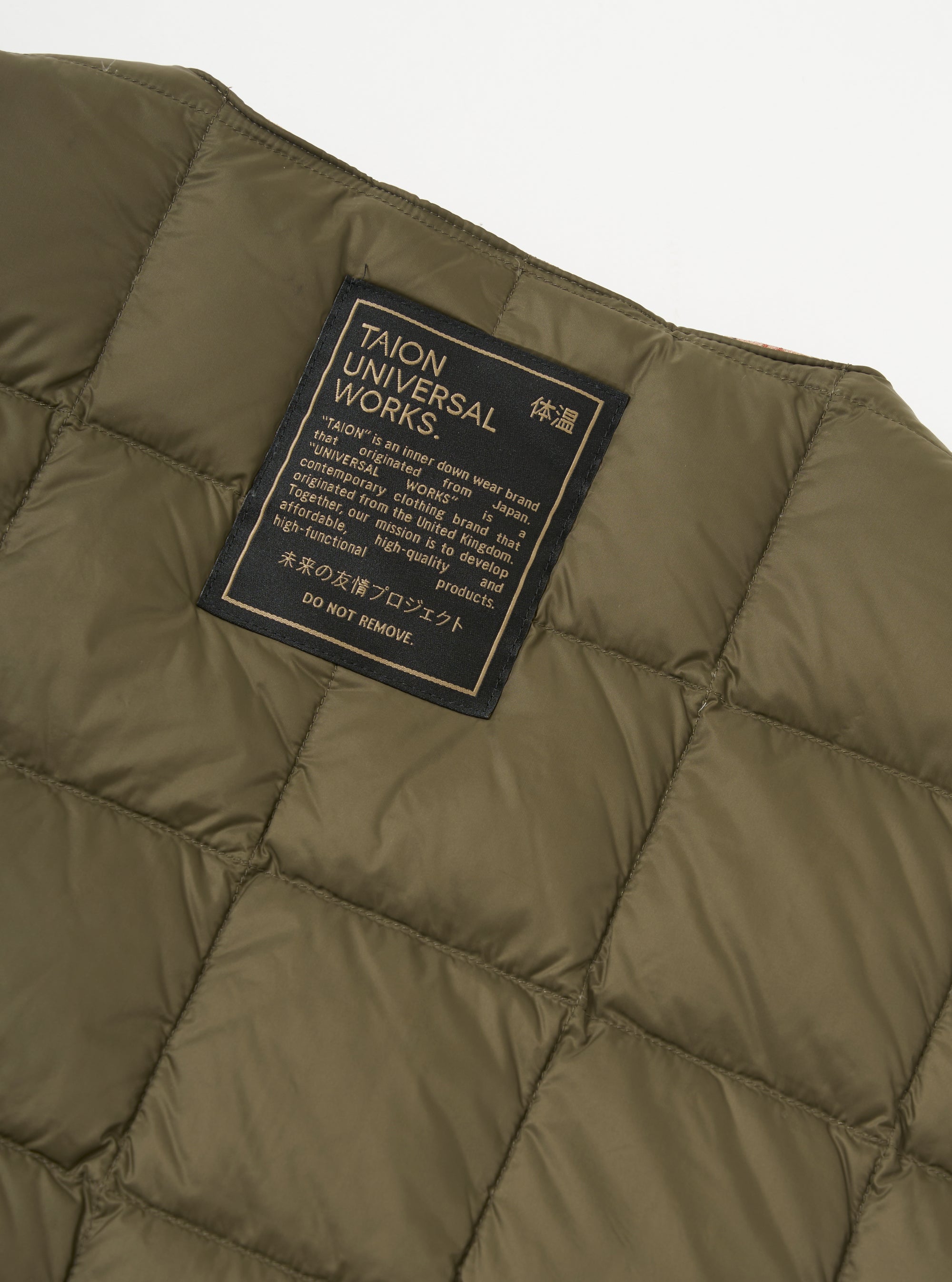 Close-up of the TAION x Universal Works Reversible Dark Olive Military Line Vest, showcasing the quilted texture and brand label on a neutral background.