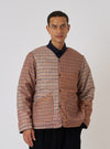 A model poses in the TAION x Universal Works Reversible Black Military Line Liner Jacket. The jacket is brown and tan houndstooth. Shot against a white backdrop.