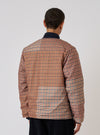 Back view of a model wearing the TAION x Universal Works Reversible Black Military Line Liner Jacket. The jacket has a brown and black houndstooth pattern. Shot against a white background.