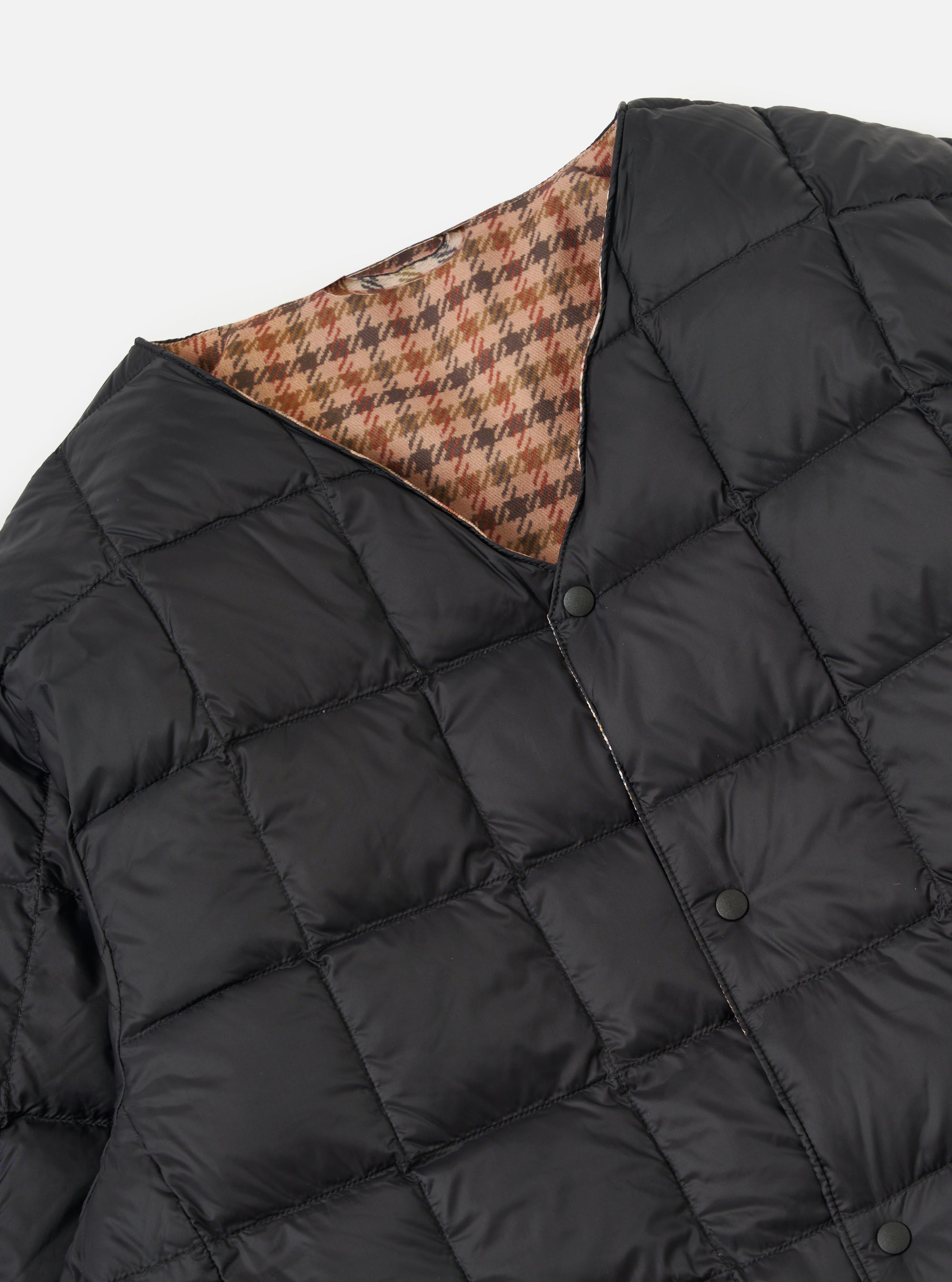 Close-up of the TAION x Universal Works Reversible Black Military Line Liner Jacket on a white background. Shows the black quilted material and the brown houndstooth pattern on the reverse side.