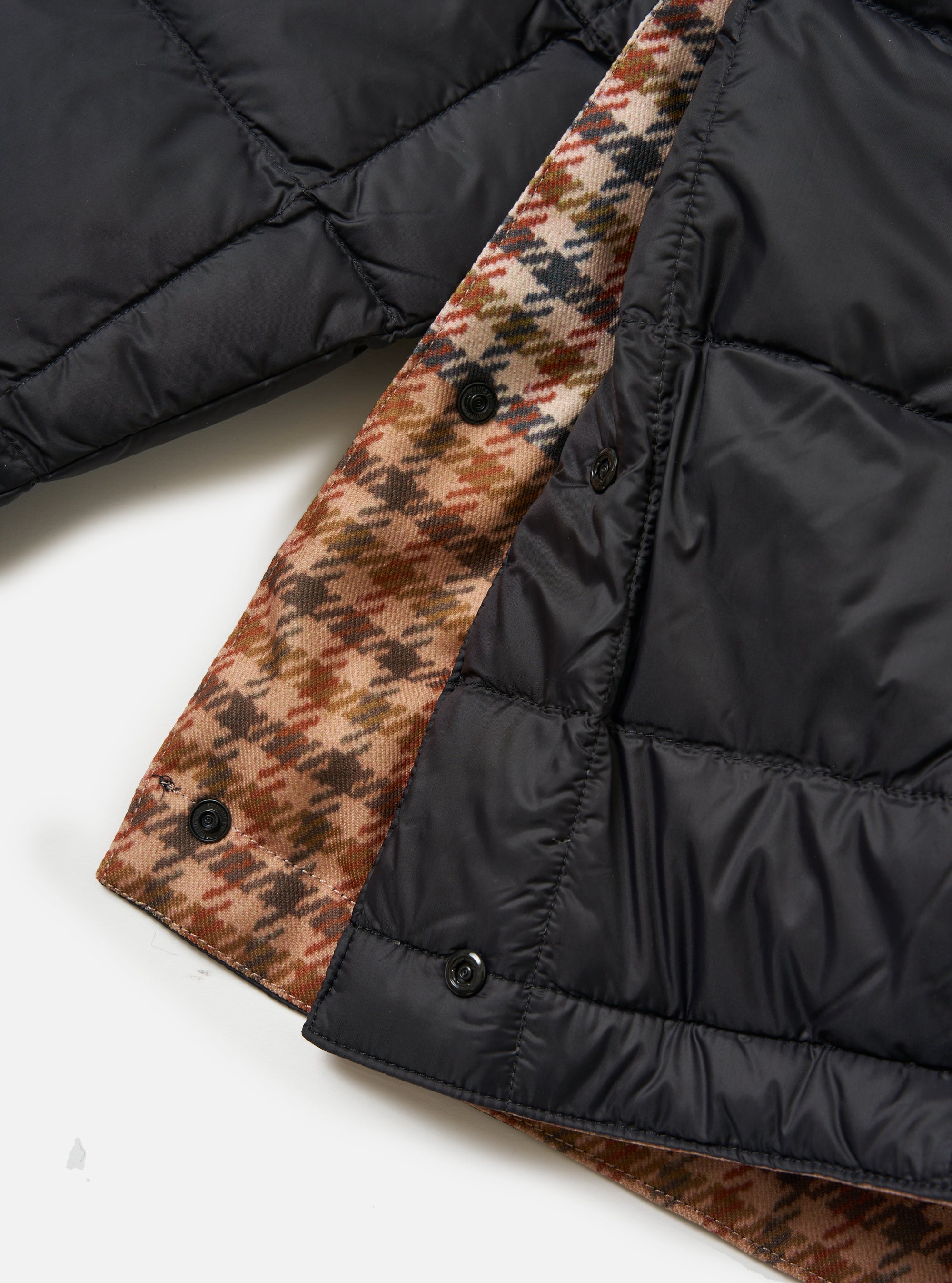 Close-up of the TAION x Universal Works Reversible Black Military Line Liner Jacket. Features black quilted nylon on one side and a brown houndstooth pattern on the other. Shot on a white background.