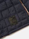 Close-up of the TAION x Universal Works Reversible Dark Navy Military Line Liner Jacket, showing the quilted dark navy material, branded label, and patterned trim on a white background.