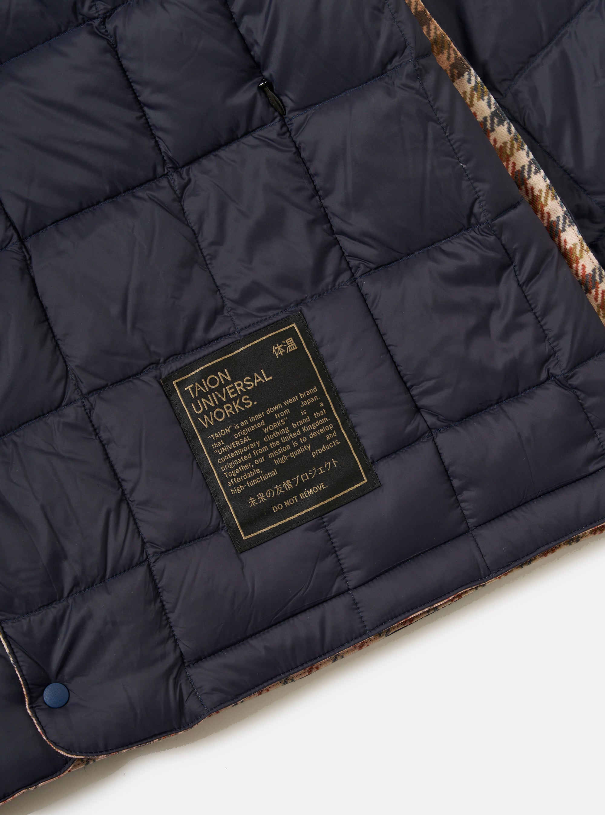 Close-up of the TAION x Universal Works Reversible Dark Navy Military Line Liner Jacket, showing the quilted dark navy material, branded label, and patterned trim on a white background.