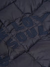 Close-up of the TAION x Universal Works Reversible Dark Navy Military Line Liner Jacket, showcasing the quilted texture and embroidered lettering on the dark navy material.