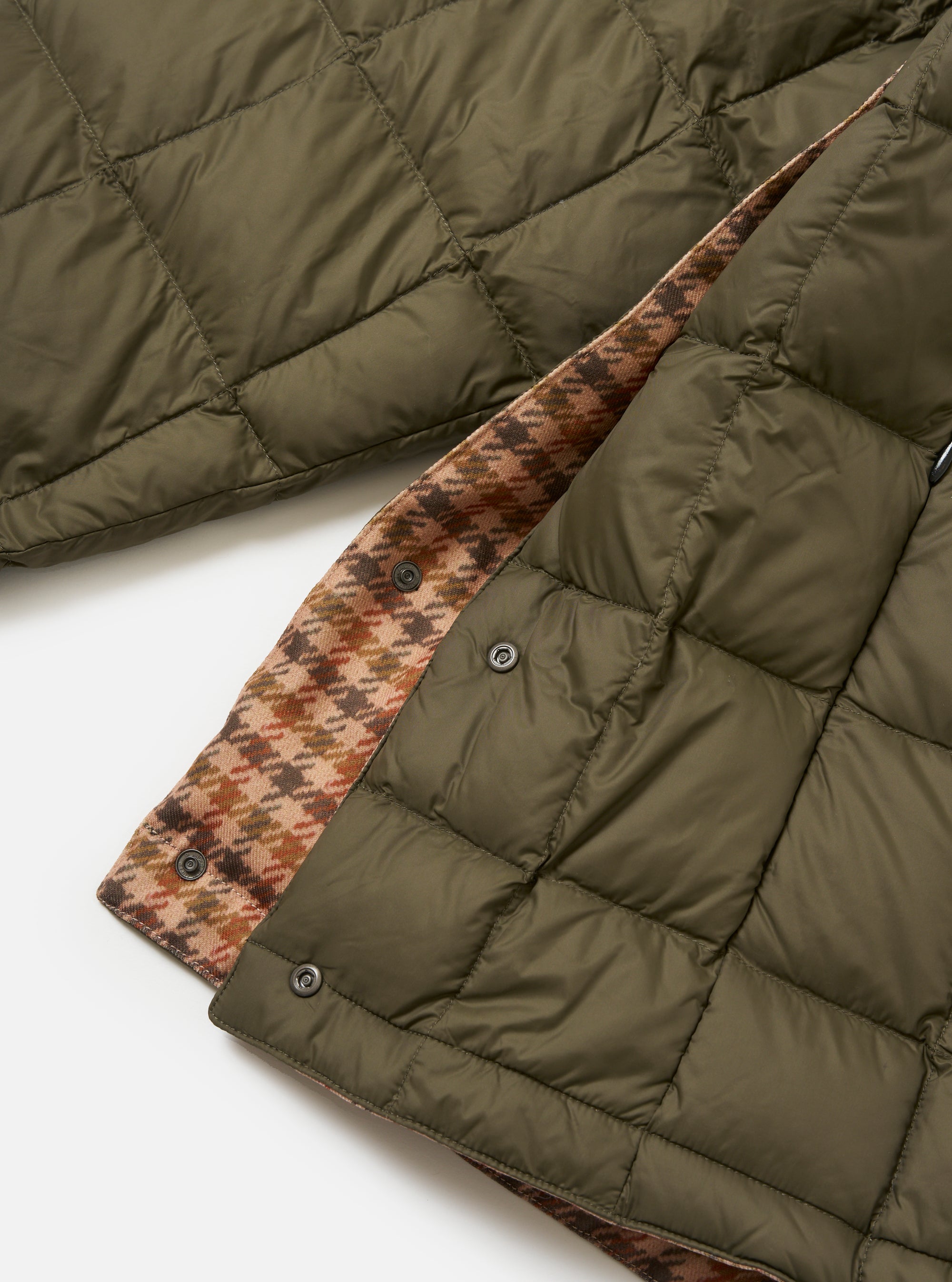 Close-up of the TAION x Universal Works Reversible Dark Olive Military Line Liner Jacket, showing the dark olive quilted material and the brown houndstooth reversible side. Shot on a white background.