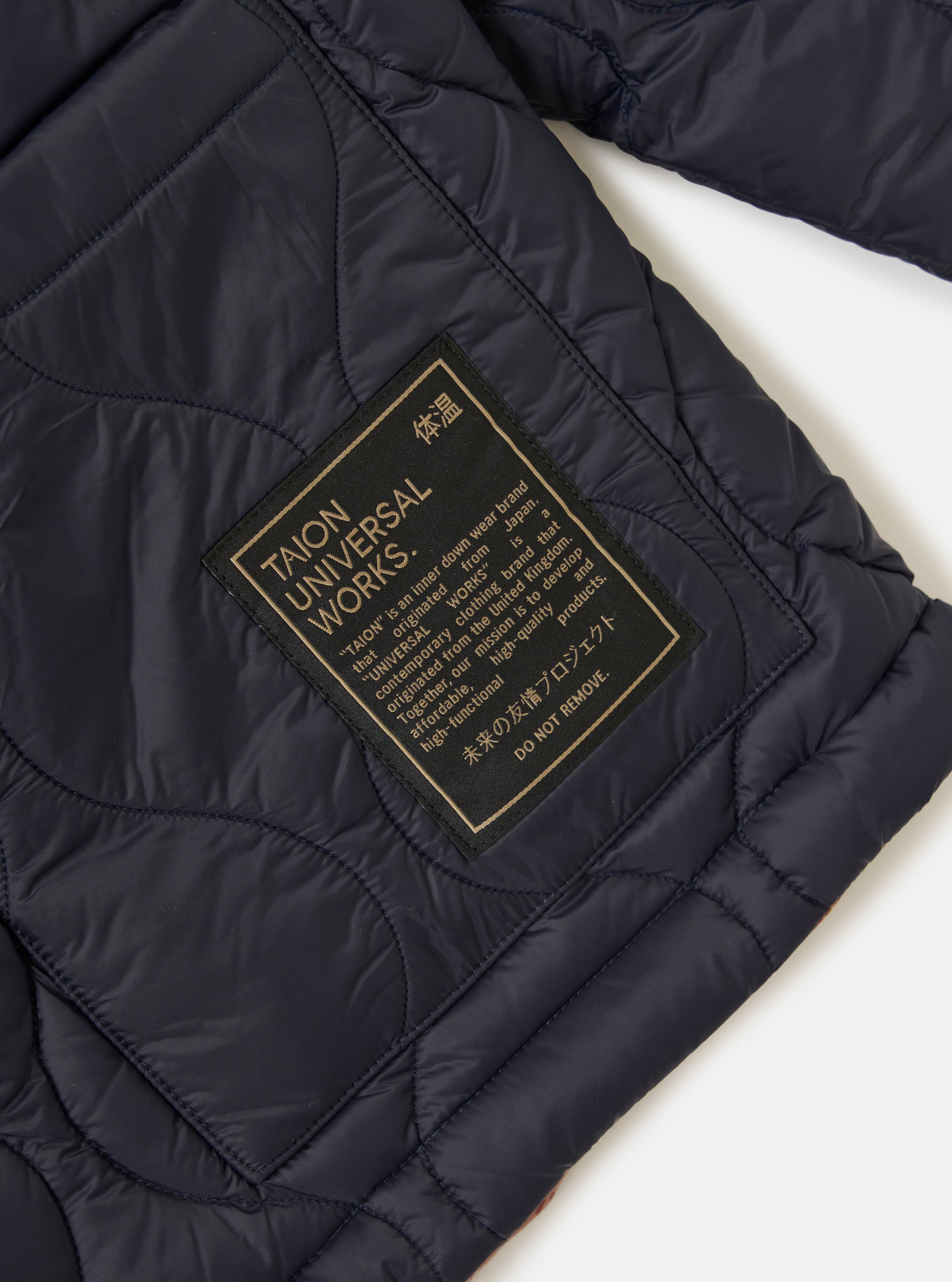 Close-up of the TAION x Universal Works Reversible Dark Navy Military Line Kyoto Work Jacket showing the quilted texture and branded patch on a white background.