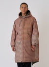 A model on a white background wears the TAION x Universal Works Reversible Dark Olive Military Line Parka. The parka has a brown and tan houndstooth pattern and a relaxed fit.