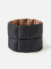 The TAION x Universal Works Reversible Black Military Line Neck Warmer. It's black quilted on the outside and brown houndstooth patterned on the inside. Shot on a white background.