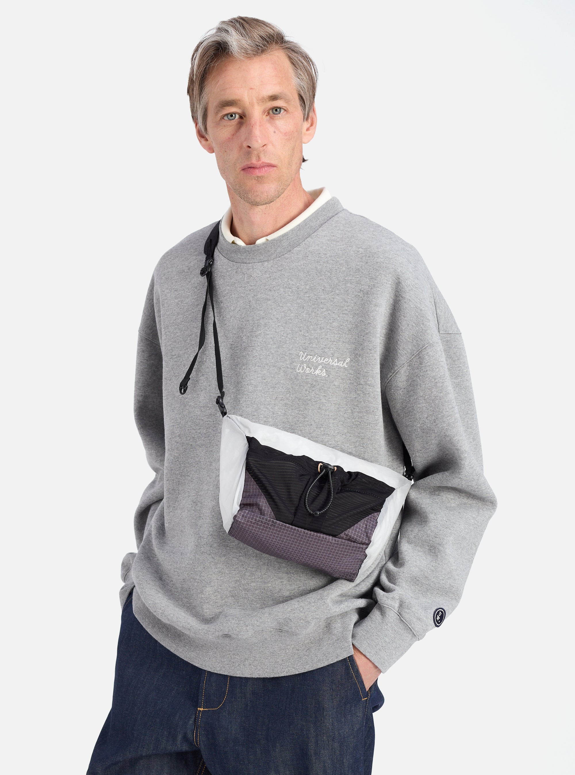 Model wears the F/CE.® White Nylon Cordura Sil Sacoche. The bag is white, black and grey. Shot in a studio on a white background.