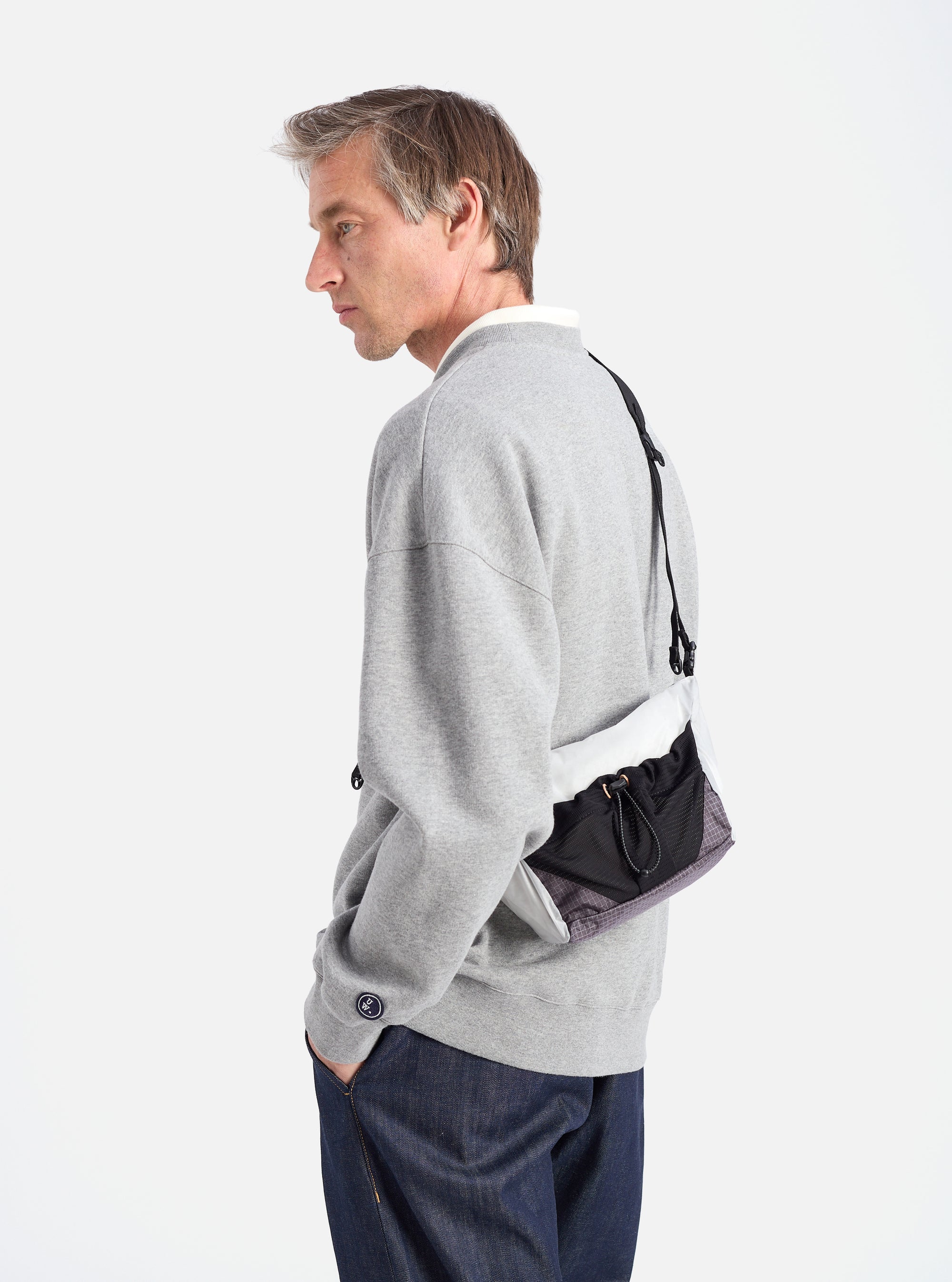 A model showcases the F/CE.® White Nylon Cordura Sil Sacoche. The bag features white, black, and gray nylon. Shot in a studio with a white background.