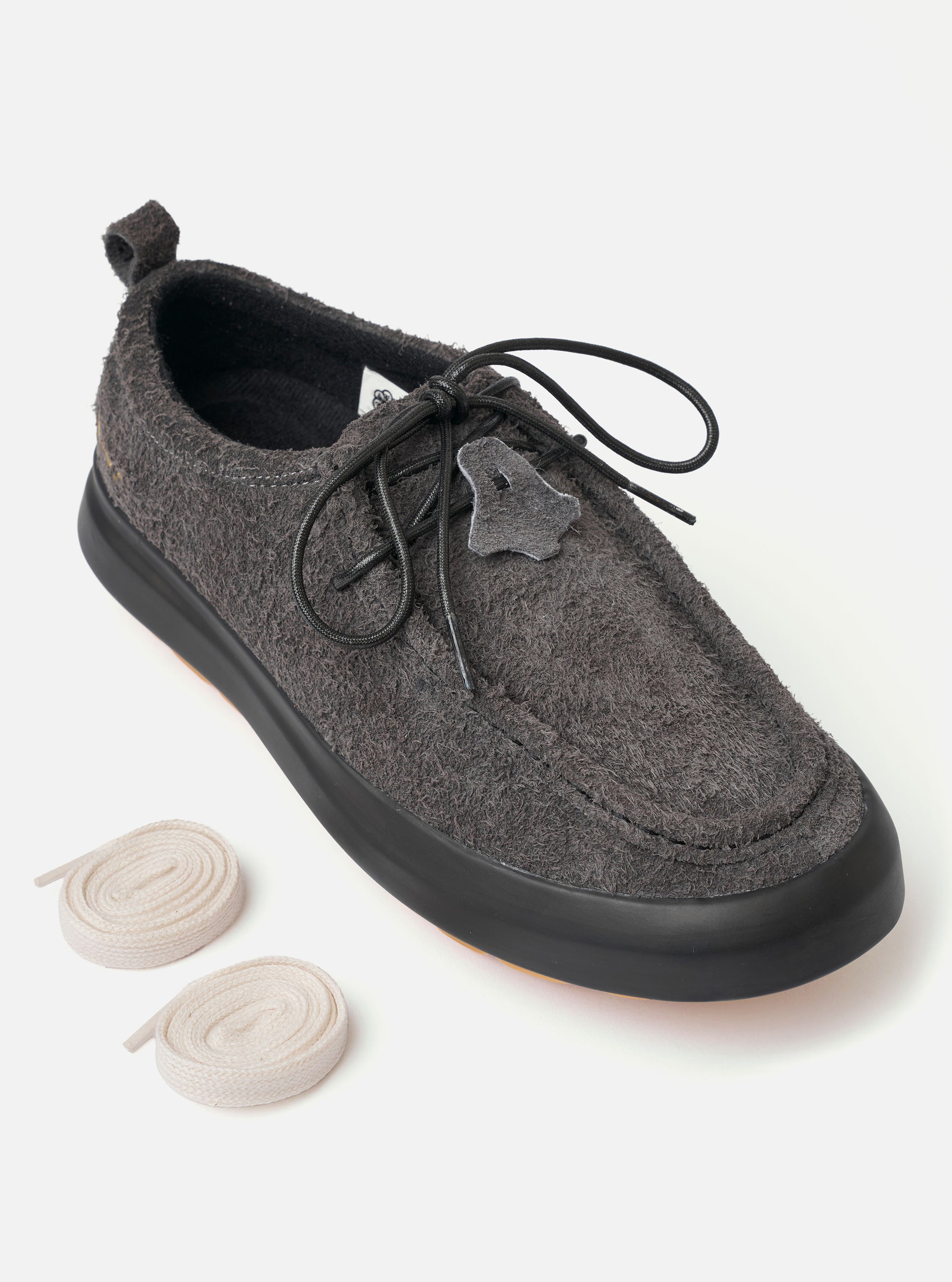 The Wander etc. FD/08 Low in Black Asphalt/Gum Hairy Suede is shown from a side profile as a flat lay against a plain white background. The shoe features a black hairy suede upper, slim black laces, and a chunky gum rubber outsole. The low-cut design and textured leather are the prominent features.