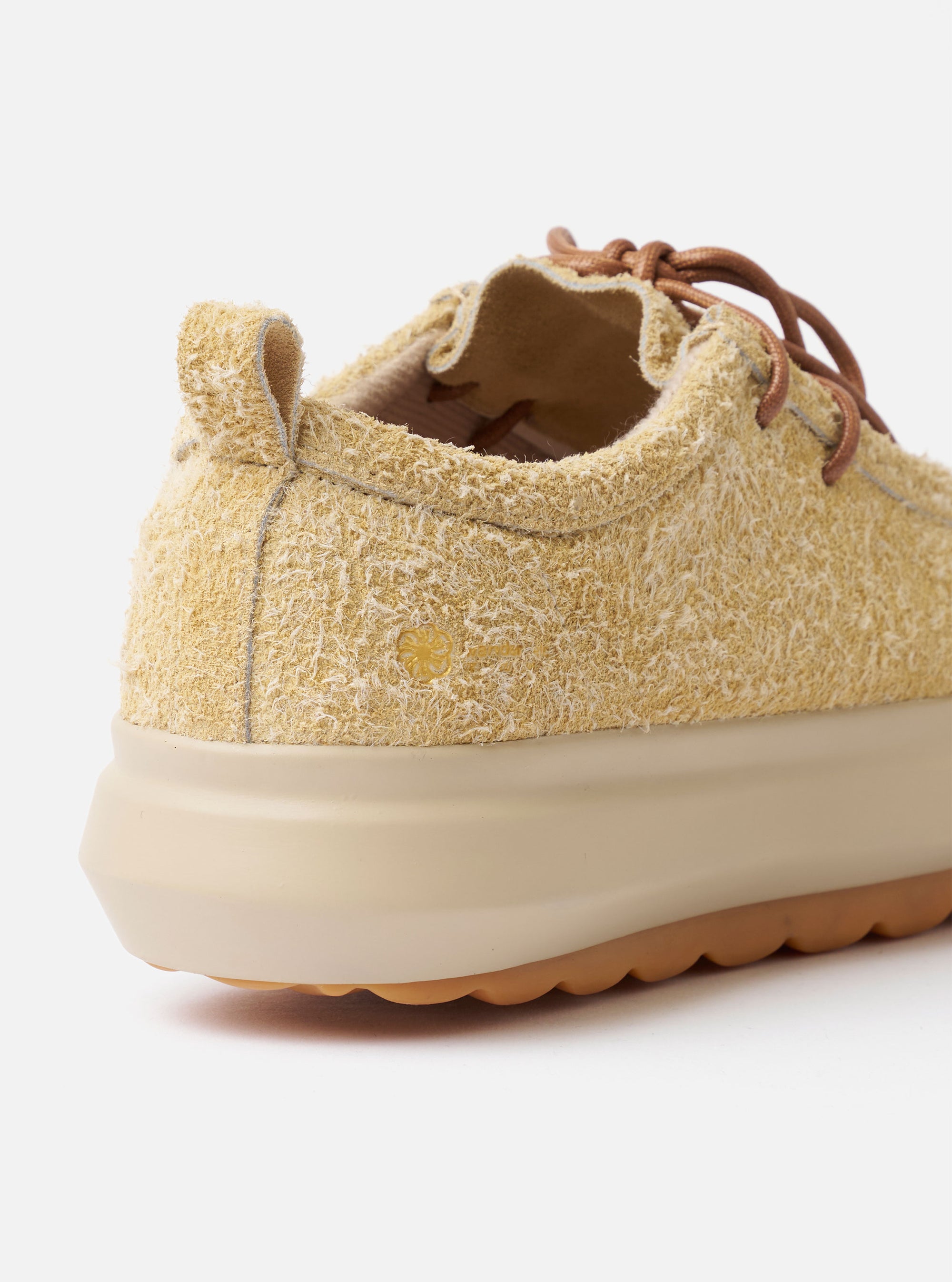 The Wander etc. FD/08 Low in Dune/Gum Hairy Suede is shown from a rear angle as a flat lay against a plain white background. The image highlights the shoe's heel, featuring a pull tab and branding, along with the thick gum-colored rubber outsole. The textured dune-colored hairy suede upper and the chunky laces are also prominent.