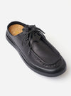 The Wander etc. Laze in Black Nappa Leather is shown from a rear three-quarter angle as a flat lay against a white background. The image highlights the backless mule design, the smooth black nappa leather upper, and the thick, chunky black outsole. The interior features a tan cork footbed with a printed logo.