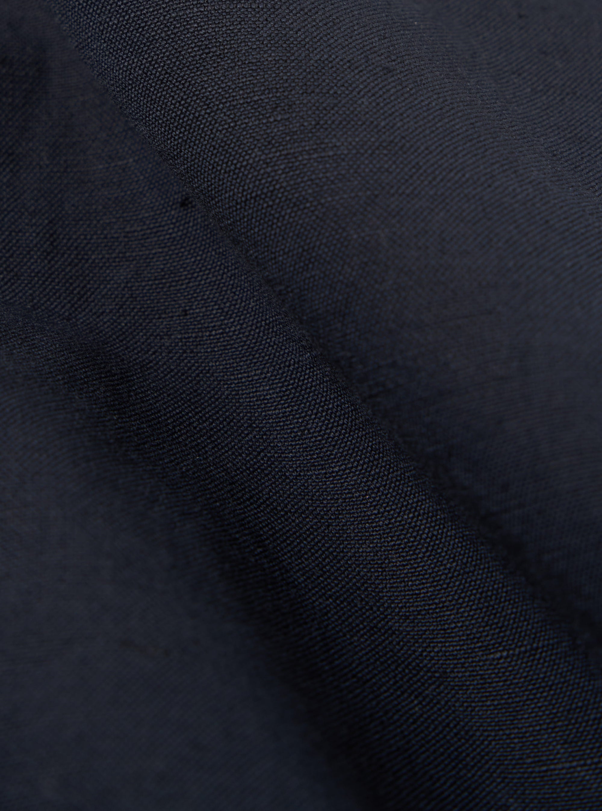 Close-up of the navy linen slub weave simple short fabric. The texture is visible, showing the weave pattern. The fabric is draped, creating shadows and highlights.